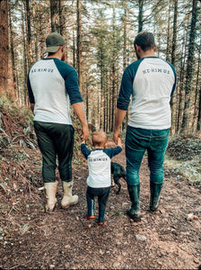 two-dads-little-boy-walking-through-forest-in-matching-t-shirts-he-him-us-logo