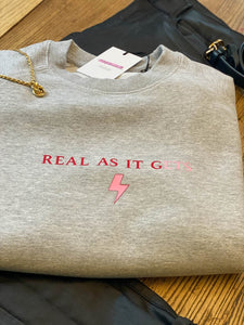 Grey-sweatshirt-close-up-slogan-Real-as-it-gets-with-pink-thunderbolt-detail